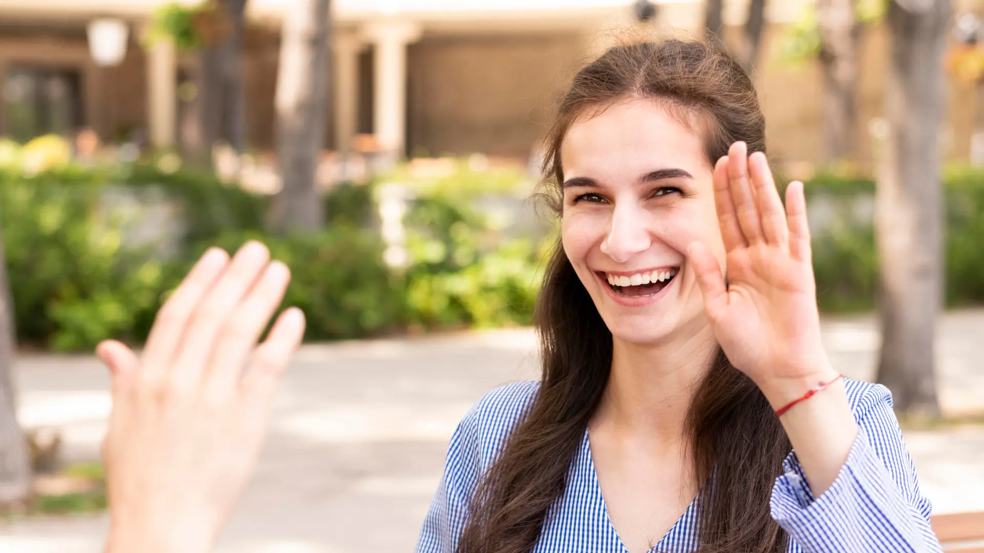 Smiling woman high-fiving outside, showing confident body language and approachable first-impression signals for interviews