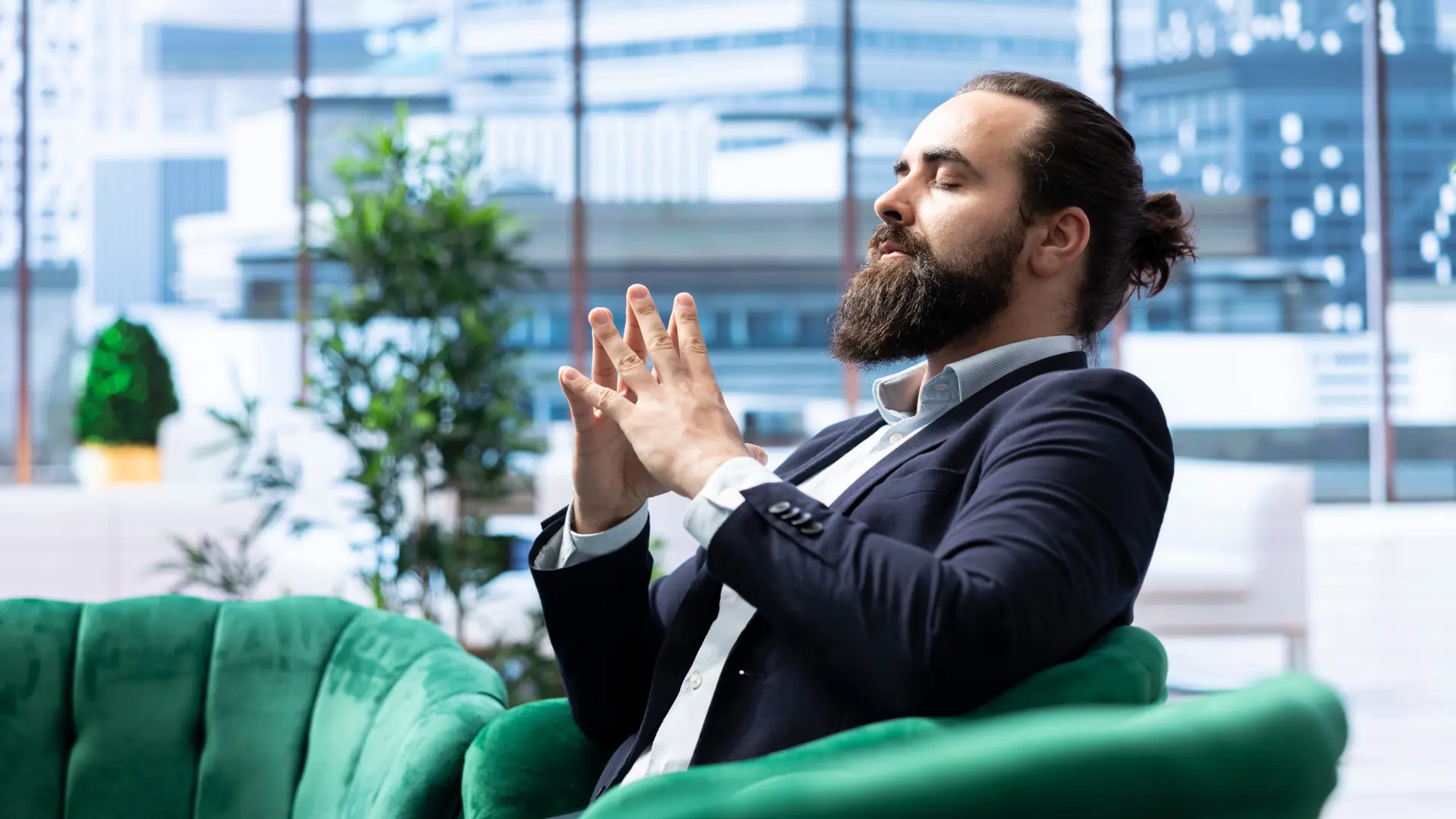 Bearded man in suit practicing confident posture and composed hand gesture on green chair in modern office for interview tips