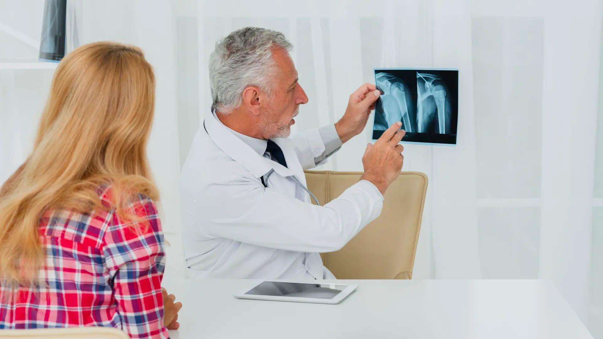 Doctor holds shoulder X-ray while explaining results to female patient, demonstrating diagnostic radiation use