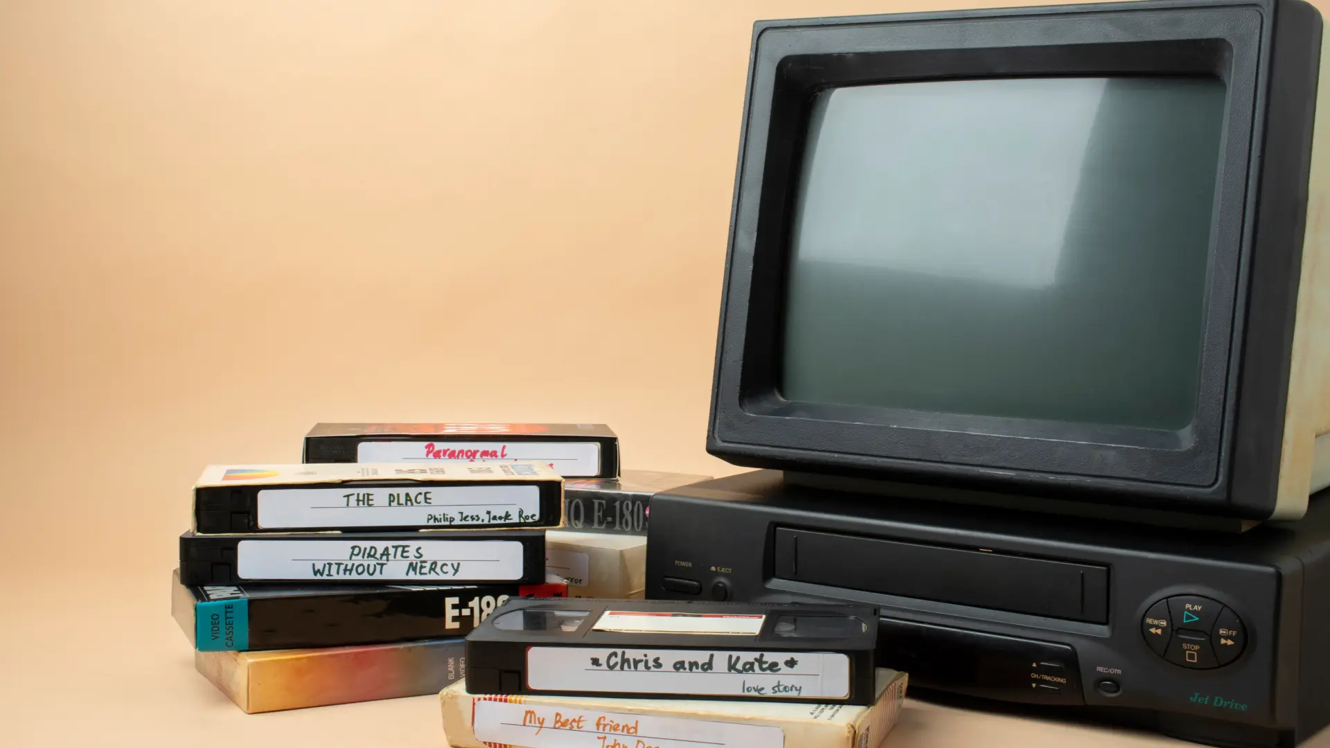 Retro CRT monitor and VCR with stacked VHS tapes on beige background illustrating early home gaming and media era